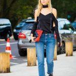 le-fashion-blog-pfw-street-style-pernille-teisbaek-black-deconstructed-blouse-with-a-wrapped-neck-open-shoulders-and-draped-sleeves-bright-red-clutch-bag-midwash-cropped-denim-with-raw